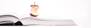 Das Foto zeigt einen angebissenen Apfel auf einem aufgeschlagenen Buch liegend.